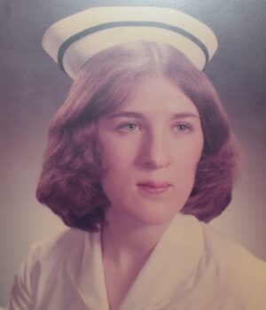 a brunette woman in a white hat with a blue stripe around it, with white skin and a white nurse's uniform.